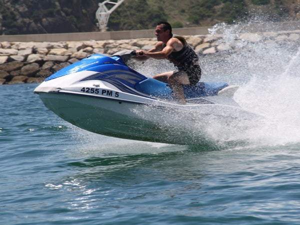 Man riding a jet ski, almost jumping from the water, with rocks behind, Albufeira.